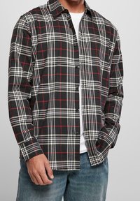 Camicia a quadri neri, bianchi e rossi con bottoni, realizzata in tessuto morbido, caratterizzata da un colletto, maniche lunghe e bottoni neri.