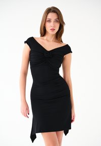 Czarna sukienka z elastycznego materiału; ma dekolt w kształcie serca, detal w postaci węzła z przodu oraz dopasowaną sylwetkę z asymetrycznym dołem.