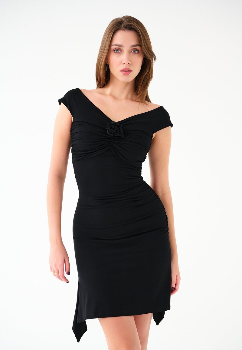 Czarna sukienka z elastycznego materiału; ma dekolt w kształcie serca, detal w postaci węzła z przodu oraz dopasowaną sylwetkę z asymetrycznym dołem.