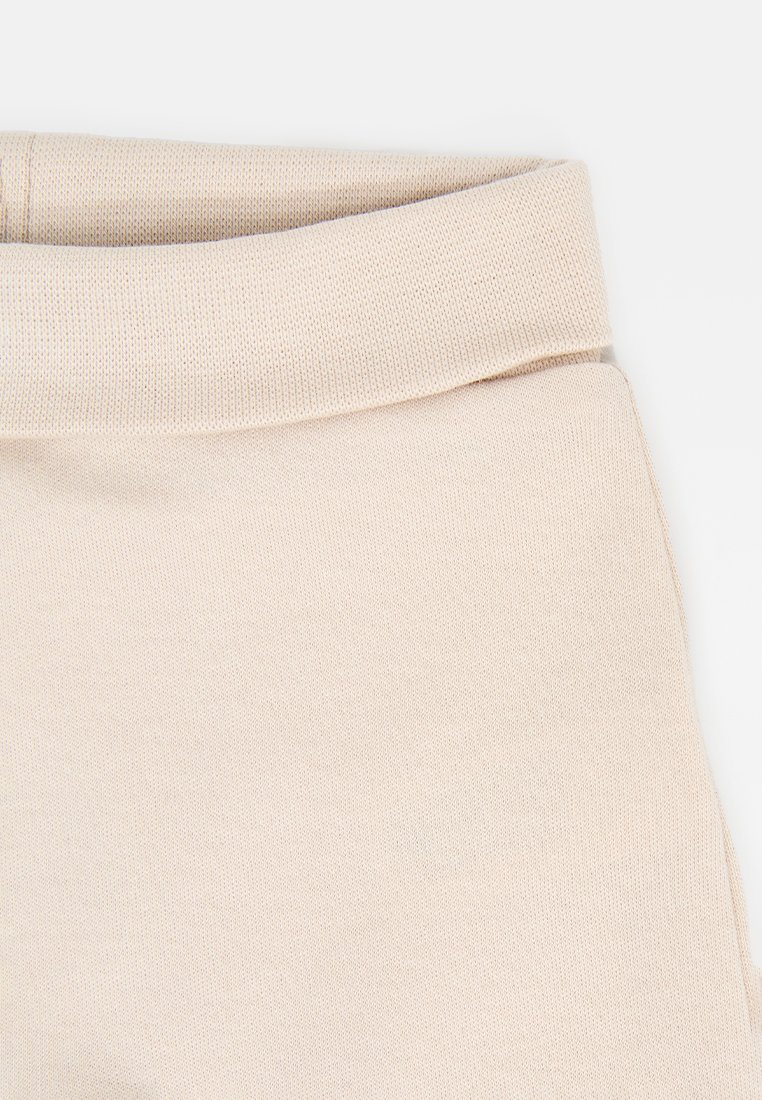 Primer plano de una tela de punto beige con un puño doblado, mostrando la textura y los detalles de costura.
