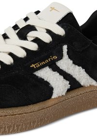Sneaker in suede nero con lacci crema, caratterizzato da morbidi accenti bianchi e una suola in gomma marrone tessurizzata. Dettaglio logo oro presente.