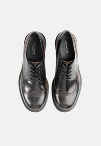 Czarne derby ze skóry z perforowanymi detalami, brązowym przeszyciem, zaokrąglonym noskiem i gładką teksturą. Wiązane, o klasycznym kroju.
