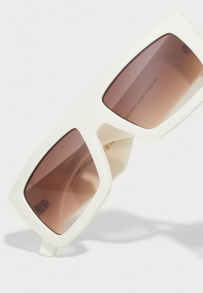 Ochelari de soare supradimensionați, albi, cu lentile maro gradient. Formă rectangulară, rame groase și branding discret pe partea interioară a brațului. Textură netedă.