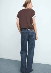 Bruine katoen t-shirt met opgerolde mouwen, gecombineerd met donkerblauwe denim jeans met een rechte snit en achterzakken. Eenvoudig, strak ontwerp.