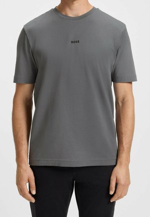 Mand iført en ensfarvet grå kortærmet T-shirt med "BOSS" trykt med små sorte bogstaver på brystet.