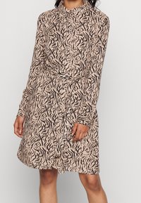 Skjortklänning i beige med ett mönster av svarta tigerränder. Har krage, långa ärmar, midjeband och knäppning fram.