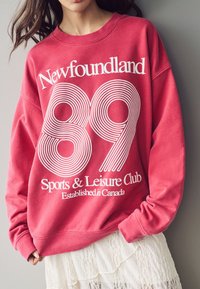 Felpa rossa in cotone con testo bianco e grafica: "Newfoundland 89 Sports & Leisure Club Fondato in Canada." Texture morbida, vestibilità rilassata.
