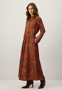 Vestido largo marrón con un patrón floral en tonos oscuros, con cierre de botones en el frente, mangas largas y bolsillos. Hecho de tela suave.