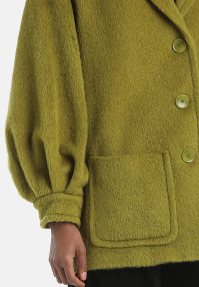 Olijfgroene wollen jack in een blend met een zachte, gestructureerde oppervlakte. Voorzien van een reverskraag, oversized mouwen en drie knopen. Enkele vozak.