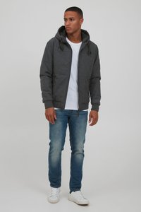Gray bomber jacket with a hood, featuring zip closure and two side pockets. Paired with a white t-shirt and blue jeans. White sneakers.