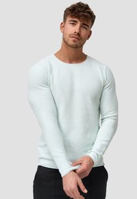 Lys mintgrøn langærmet pullover trøje med et tekstureret strikkemønster, rund halsudskæring og tætsiddende ærmer, iført med sorte bukser.