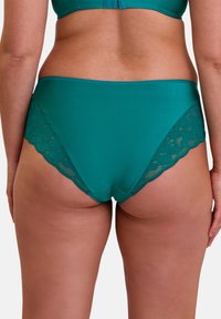 Culotte hipster teal en tissu lisse avec des détails en dentelle festonnée sur les côtés. Taille élastique avec un dos sans couture.