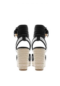Černé espadrilky na podpatku s tkanými lanovými klíny, úvazky kolem kotníků a síťovinovými akcenty. Vyznačují se pevným tkaným texturováním a jednobarevným černým svrškem.