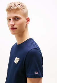 Tamsiai mėlynas medvilninis marškinėliai su apykakle. Ziemas крем logo ant krūtinės ir mažas raudonas, baltas ir mėlynas ženklas ant rankovės.