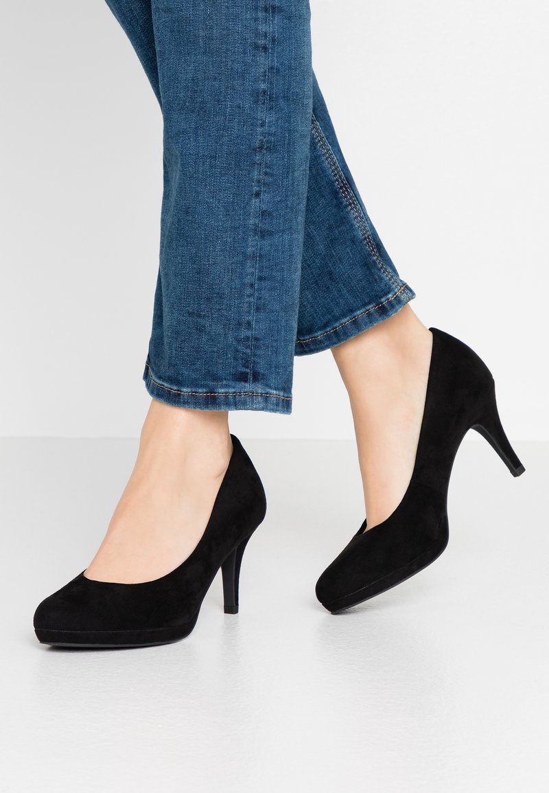 Escarpins en suède noir avec un bout arrondi et un talon aiguille de 7,5 cm, associés à un jean bleu, présentant une texture subtile et des lignes épurées.