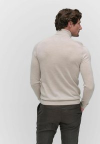 Beige coltrui met geribbelde manchetten en zoom, gedragen met donkergrijze broek. Glad textuur, aangesloten ontwerp, minimalistische stijl.