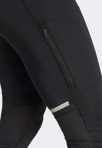 Black athletic leggings featuring a zippered pocket, textured mesh panels, and reflective accents along the thigh for visibility.