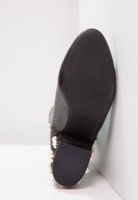 Schwarze Lederknöchelstiefel mit runder Zehenform, strukturiertem Gummisohle und Perlenverzierungen an der Ferse. Glatte Oberfläche, keine sichtbaren Muster.