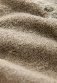 Beiger Wollstoff mit einer weichen, strukturierten Oberfläche, die zarte Farbvariationen und ein natürliches, leicht fuzziges Aussehen zeigt.