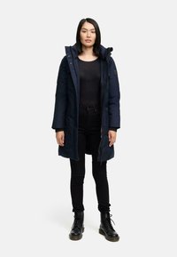 Navy long winter coat with a hood, front zipper, and snap closures, paired with black fitted top, jeans, and black lace-up ankle boots.