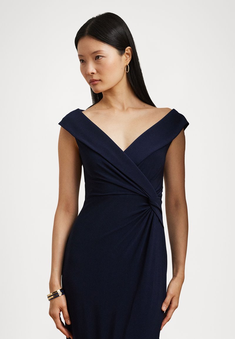 Abito blu navy con maniche scese sulle spalle, caratterizzato da un dettaglio anteriore attorcigliato e una silhouette aderente realizzata in tessuto liscio.