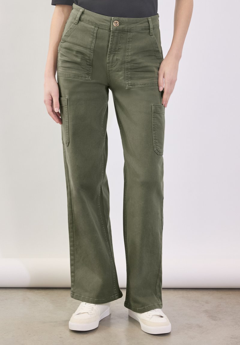 Groene cargobroek met een hoge taille, meerdere zakken en een recht model. Gemaakt van een zachte, duurzame stof. Witte sneakers zijn zichtbaar.