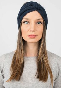 Fascia in maglia blu navy con un design attorcigliato. Texture morbida e forma aderente. Indossata da una persona con capelli lunghi e lisci.