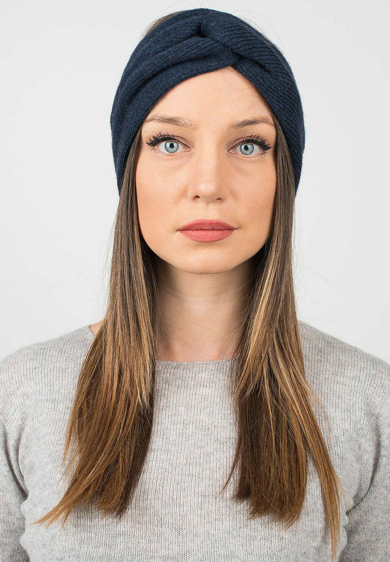 Fascia in maglia blu navy con un design attorcigliato. Texture morbida e forma aderente. Indossata da una persona con capelli lunghi e lisci.