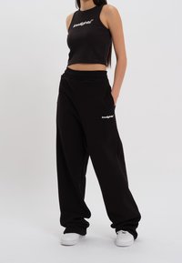 Top cropped nero e pantaloni tuta neri dal taglio morbido, entrambi con dettagli del logo bianco. Tessuto liscio e design rilassato.