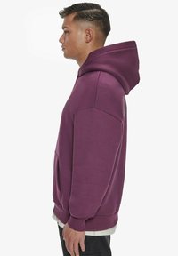 Violet sweatshirt su kengūrinėmis kišenėmis, smulkiai susiūtomis rankovėmis ir tiesiu apvadu. Lygus paviršius, laisvas siluetas ir gobtuvas. Minimalus prekinis ženklas šone.