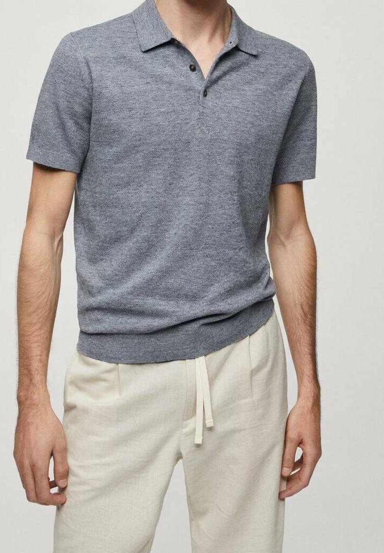 Polo shirt gris à manches courtes avec une finition texturée, doté d'une patte de boutonnage et d'une taille ajustée. Porté avec un pantalon beige clair.