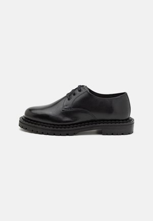Chaussure noire en cuir à lacets avec semelle épaisse crantée, dessus lisse et bout arrondi, présentée de profil sur fond blanc.