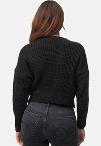 Svart våffelstickad cropped tröja med ribbad halsringning och lös passform, ihop med mörka jeans med hög midja och bakfickor.