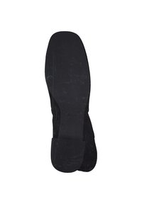 Chaussure en suède noire avec une semelle en caoutchouc plate, présentant une texture lisse et sans motifs visibles. Le talon a un accent en caoutchouc légèrement surélevé.