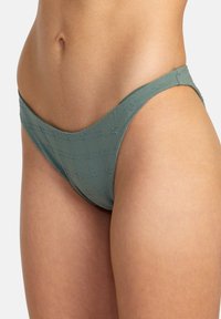 Grön bikinitrosa av texturerad tyg med ett delikat mönster. Designad med låg midja och tunna sidostrapsar för minimal täckning.