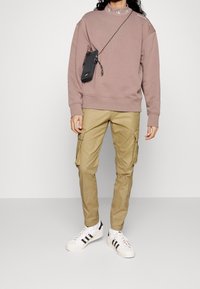 Brun sweatshirt med broderad krage, kombinerad med khaki cargobyxor och vita sneakers med svarta ränder. Liten svart axelväska.