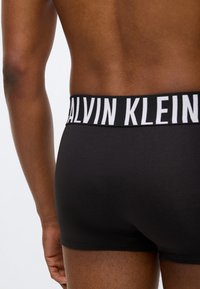 Μαύρα βαμβακερά μποξεράκια με φαρδύ ελαστικό μέσο με λευκή επιγραφή "CALVIN KLEIN", λεία υφή και εφαρμοστή σχεδίαση που δείχνει την πίσω όψη.
