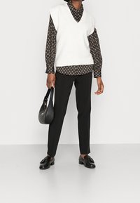 Vit stickad väst med v-ringning, brun mönstrad långärmad skjorta, svarta kostymbyxor, svart axelväska och svarta loafers.