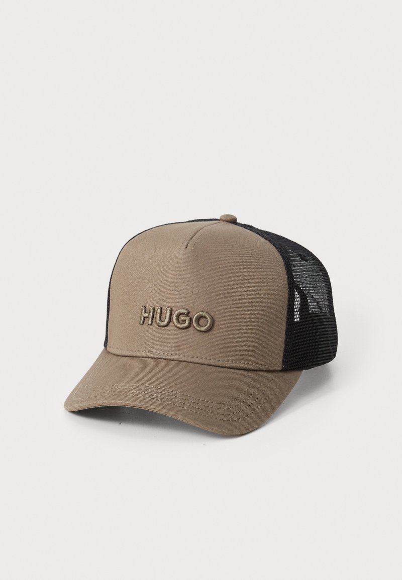 Căciulă maro cu o margine curbată și spate din plasă neagră. Prezintă logo-ul brodat "HUGO" pe față. Fabricată dintr-un material textil cu textură netedă.