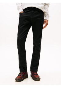 Pantalones de mezclilla negros con un diseño de pierna recta, que cuentan con bolsillos laterales y cierre de botón. Combinados con zapatillas multicolores texturizadas.