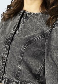 Chaqueta de mezclilla gris con cierre de botones en la parte delantera, tejido texturizado, costuras distintas y cuello redondeado; diseño corto con detalles de costura visibles.