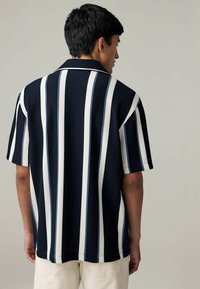 Camisa de manga corta con rayas verticales en azul marino y blanco, textura acanalada y cuello clásico. Adecuada para un estilo casual.