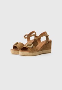 Sandali con zeppa in suede beige con due cinturini e dettagli in punta tonda. Presentano una suola in juta intrecciata e un design aperto sulla punta.