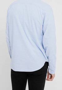 Light blue long-sleeve shirt with a straight hem, buttoned cuffs, and a soft fabric. Features a back yoke and a relaxed fit.