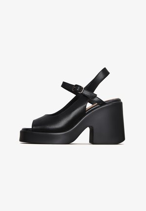 Black leather platform sandals featuring a peep toe, adjustable ankle strap, and chunky heel. Smooth texture with minimal accents.