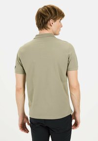Kahakifarbenes Poloshirt mit weicher Textur, kurzen Ärmeln und klassischem Kragen. Verfügt über ein kleines Logo am linken Ärmel.