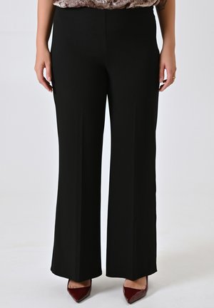 Pantaloni neri a gamba larga realizzati in tessuto morbido con vita alta. Abbinati a tacchi maroon a punta. Nessuna tasca o dettaglio visibile.