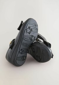 Sandales noires avec une finition brillante et des semelles en caoutchouc texturé présentant des motifs d'étoiles, des sangles réglables et des accents métalliques.