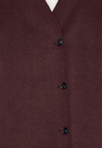 Dark maroon wool coat with a V-shaped neckline and three visible black buttons down the front.
