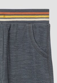 Graue Ripp-Hosen mit einem gestreiften Bund in Orange, Gelb und Weiß. Verfügt über seitliche Taschen und strukturierter Stoff.